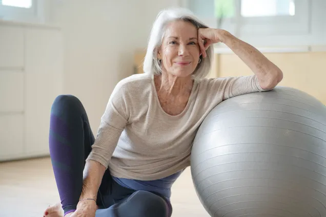 femme aux cheveux gris, assise avec un ballon d'exercice