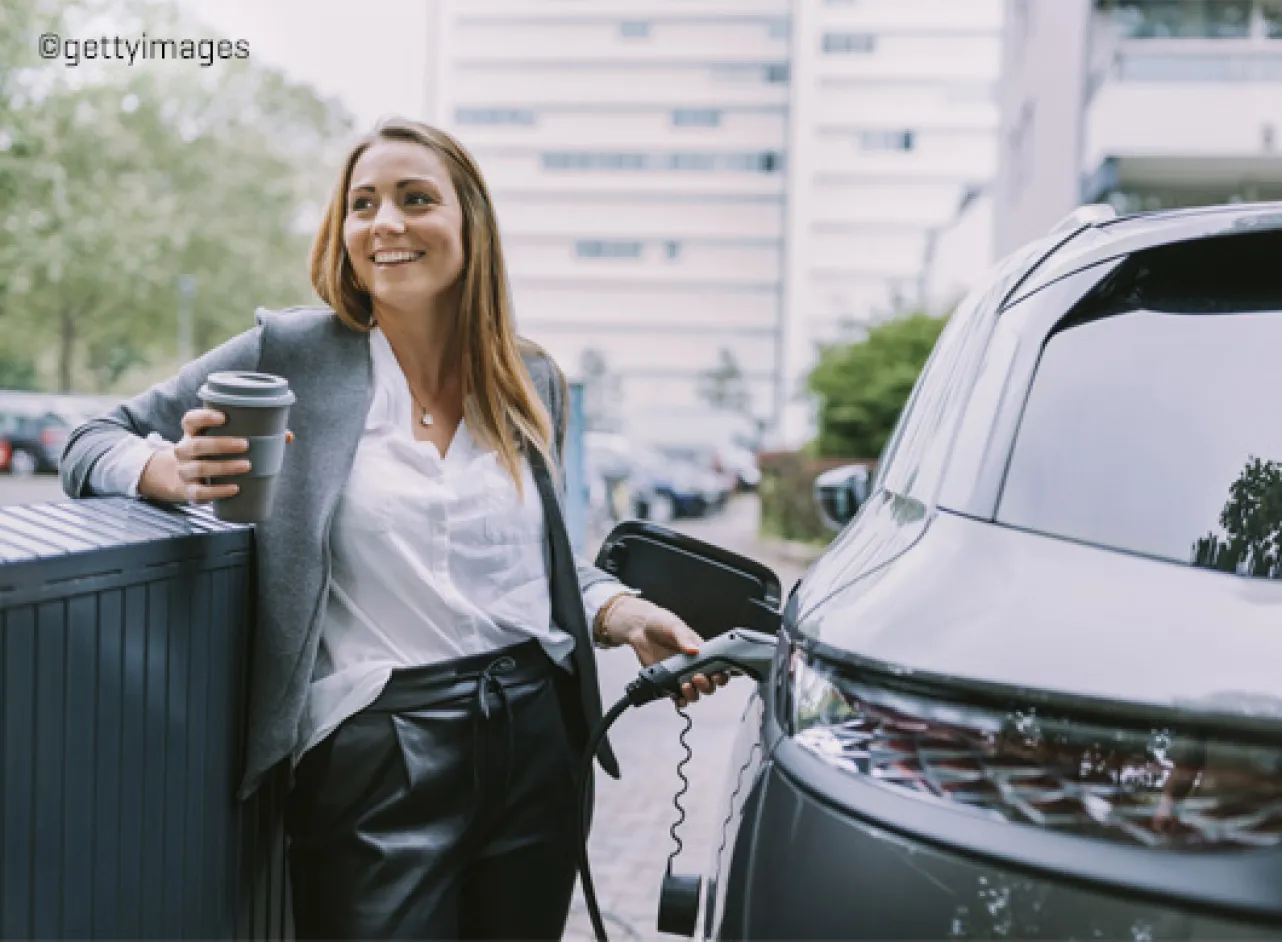 Une jeune fille recharge une voiture électrique avec du café dans l'autre main